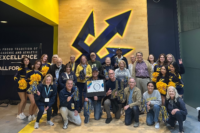 Members from Osher Lifelong Learning Institute posing with Triton Athletics staff in front of a UC San Diego trident