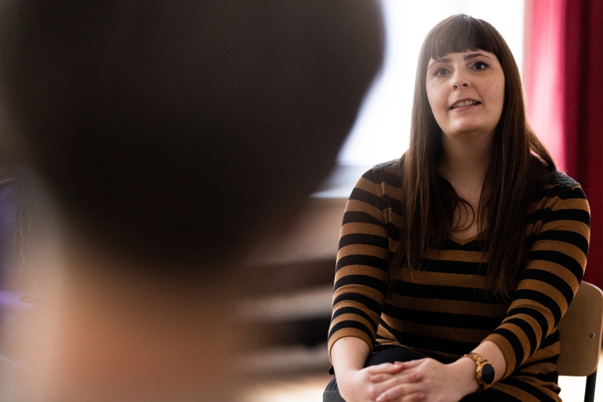 dark haired, seated woman counseling someone seated across from her who is only seen from the back