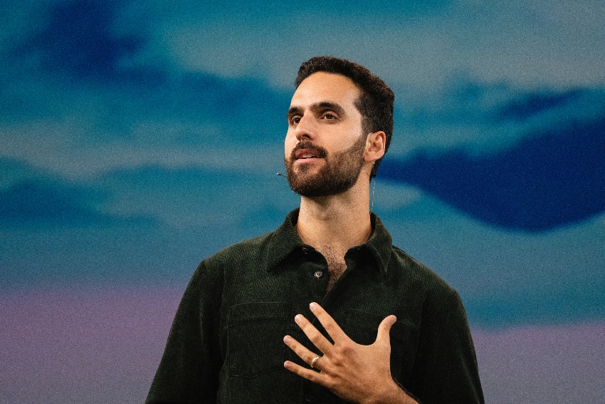 Author Simone Stolzoff presents from a stage, looking up towards the sky, with a colorful background behind him