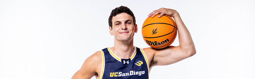 Tyson Dunn wears UC San Diego Basketball jersey and cradles a basketball in his left arm